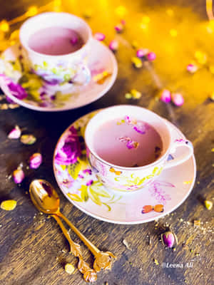 兩個花卉圖案的茶杯，裝有粉紅茶和玫瑰花瓣，放在木桌上，配有金黃色湯匙。 — Galaxy Z Fold 8 壁紙