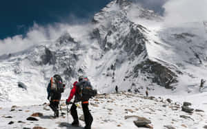 兩名登山者在多雲的天空下攀登白雪覆蓋的山脊。