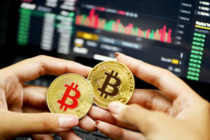 兩枚金色比特幣握在手中，後面有交易屏幕。