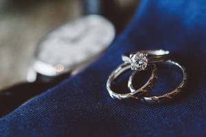 兩枚結婚戒指，帶鑽石和紋理戒環，在藍色布料上，手錶附近。