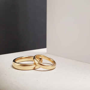 兩枚金色結婚戒指交織在白色表面上，黑白背景。 — 1:1 壁紙