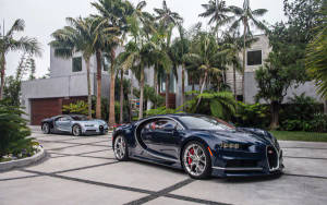 兩輛Bugatti超級跑車停泊在瓷磚車道上，背景有棕櫚樹和現代房屋。