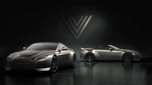 兩輛啞光灰色 Aston Martin 跑車在黑暗的攝影棚中，配有聚光燈和標誌。