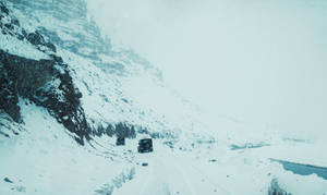 兩輛貨車在結冰河流旁的積雪山路上行駛。 — 汽車 壁紙