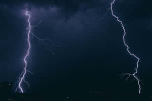 兩道明亮的閃電照亮了城市上方暴風雨的夜空。 — 雷暴 壁紙