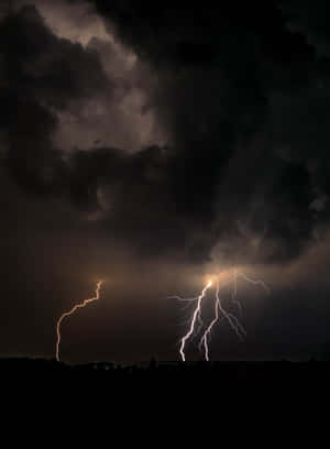 兩道明亮的閃電照亮了暴風雨夜空中黑暗山丘的上方。 — 雷暴 壁紙