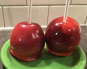 廚房裡綠色盤子上的兩顆插在棒上的紅色糖蘋果。 — 5:4 壁紙