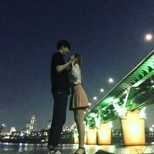 夜晚，一對情侶在燈光璀璨的橋下擁抱，背景是城市燈光。 — 情侶 壁紙