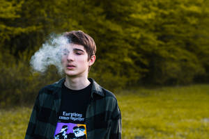 年輕男子在綠色森林中呼出煙霧。