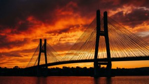 日落時分，一座現代斜拉橋，火紅橙色天空，平靜水面倒影