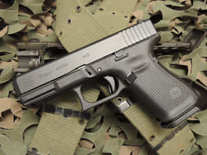 一把黑色Glock 19 Gen5手槍放在迷彩布料上，有明顯標記和縫線。 — 槍 壁紙