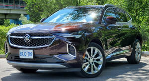 栗色Buick SUV在陽光明媚的日子停車，背景有綠樹和橋樑。