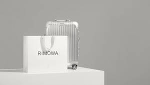 銀色Rimowa行李箱和品牌紙袋放在白色底座上。