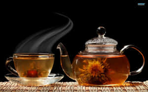 玻璃茶壺和杯子，裝有冒煙的花草茶和盛開的花朵，放在編織墊上。 — AMOLED 壁紙
