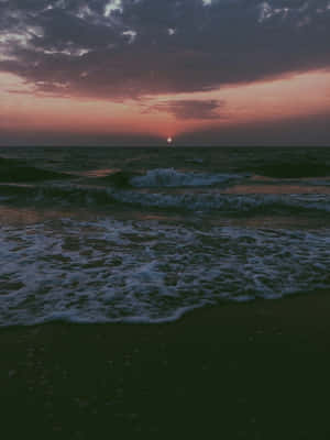 海洋上的夕陽，海浪拍打深色海灘。