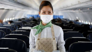 戴着口罩和圍巾的空中服務員站在空蕩蕩的飛機艙內。