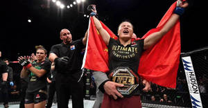 女性MMA拳手在八角籠中手持旗幟和腰帶慶祝冠軍勝利。