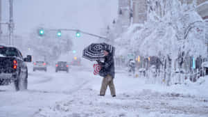 在冬季風暴中撐傘穿過積雪街道的人。