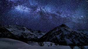 在可見銀河系的星空下，白雪覆蓋的山峰。