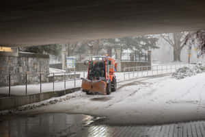 橙色掃雪車在混凝土高架橋下清理積雪。 — MacBook Pro 14 壁紙