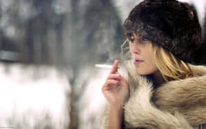穿著毛大衣和帽子的女性在雪白的冬日場景中抽煙。