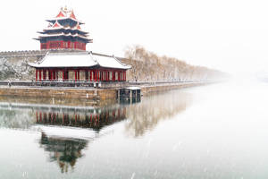 冬日平靜水面上倒映的積雪中式亭台。
