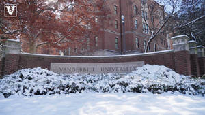 白雪覆蓋的灌木叢和磚牆，校園建築前有 Vanderbilt University 標誌。