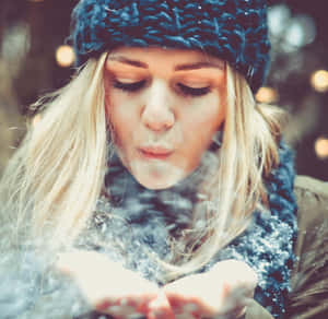 金髮女性戴著藍色針織帽，在冬夜從手中吹出雪花。 — 冬天 壁紙