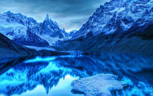 積雪的山峰倒映在平靜的藍色湖面上，在黃昏時分。