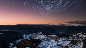 星軌在暮色中掠過雪覆蓋的山景。