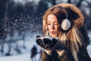 女性在冬季公園中戴著耳罩和手套吹雪。