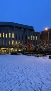 雪地庭院，腳印通往燈火通明的建築和裝飾樹木，黃昏時分。