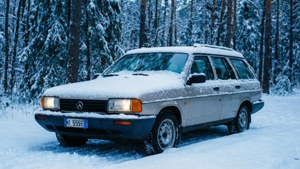 銀色旅行車被雪覆蓋，停泊在雪松林中。