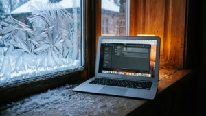 積雪窗台上的手提電腦，帶有霜花圖案和溫暖的室內光線。 — MacBook 壁紙
