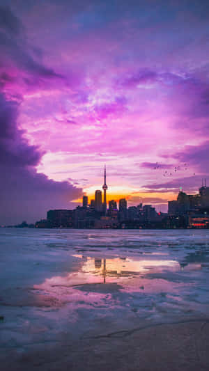 冰封的湖面倒映著多倫多天際線上空紫色的日落，以及 CN Tower。