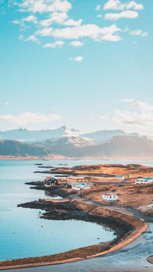 沿海村莊，房屋沿著平靜的海灣，遠處有積雪的山峰。