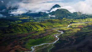 一條蜿蜒的河流流經鬱鬱蔥蔥的綠色和棕色火山山谷，背景是山脈。