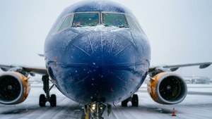 藍色飛機配備橙色引擎在降雪時停在積雪的跑道上。
