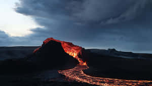 在暴風雨的天空下，黃昏時分的火山爆發中熔岩流出。 — 冰島 壁紙
