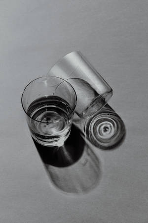 兩個玻璃杯，一個直立，一個傾倒，在灰色表面上投射陰影