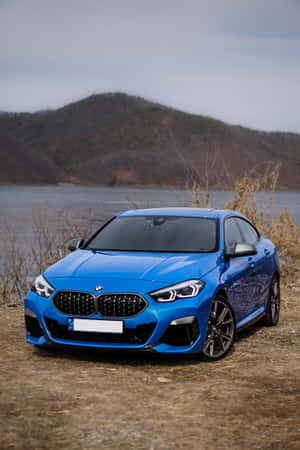 黃昏時分，藍色BMW雙門跑車停泊在湖邊，背景有山丘。