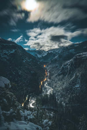 夜晚白雪覆蓋的山谷，有發光的道路燈光和條紋雲。 — 肖像 壁紙