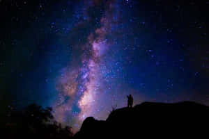人站在山丘上，星空下可見銀河