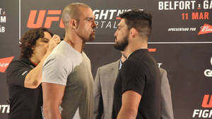 兩名男性UFC拳手在稱重活動中面對面站立，裁判調整其中一人的襯衫。