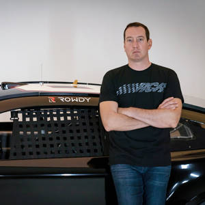 身穿黑色遙控車T恤的男子站在帶有「ROWDY」標誌的黑色賽車旁。