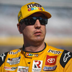 NASCAR車手身穿黃色M&M's賽車裝備，戴著太陽眼鏡在賽道上。