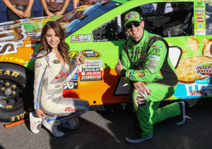 NASCAR車手和模型在陽光明媚的日子裡在一輛色彩繽紛的賽車旁擺姿勢。