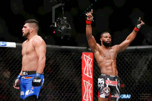 八角籠內兩名MMA拳手，一名勝利高舉雙臂，另一名在場館燈光下垂頭喪氣地站着。
