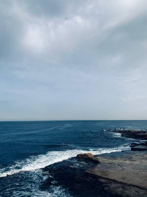 人們站在岩石碼頭上，海浪拍打著黑色的火山岩，天空多雲。 — 海浪 壁紙