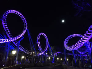 夜晚明亮的月亮下，紫色燈光過山車的迴圈。